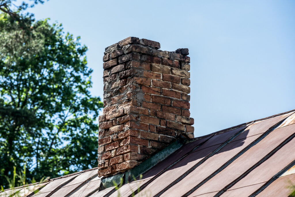 Old brick chimney in need of repair on a roof.